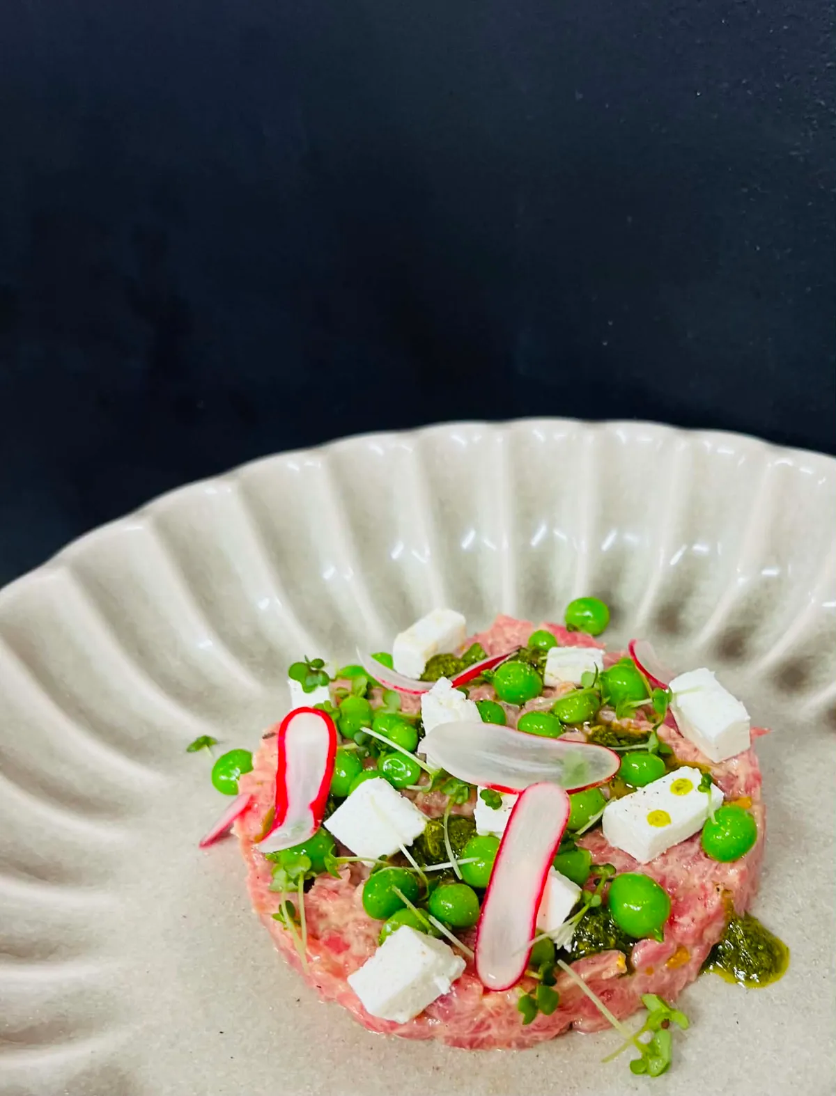 Tartare dressé avec radis, petits pois et jeunes pousses dans une assiette claire